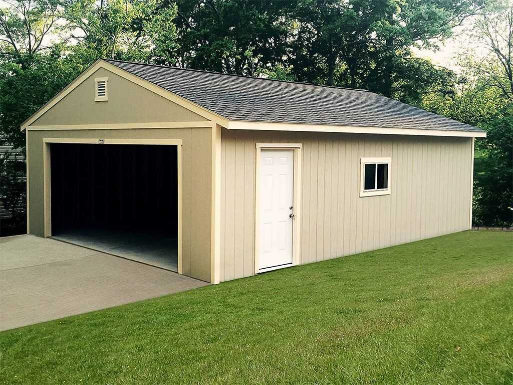 A Sundance detached garage with an open entrance, side door, and small window, set on a grassy lawn with trees in the background.