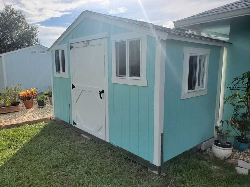 SR600 light blue shed with white trim and a double door, situated beside a house in a grassy yard