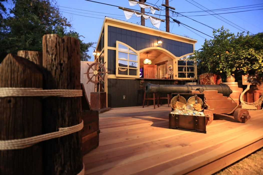 A pirate-themed outdoor space with a wooden deck, cannon, ship's wheel, and a treasure chest
