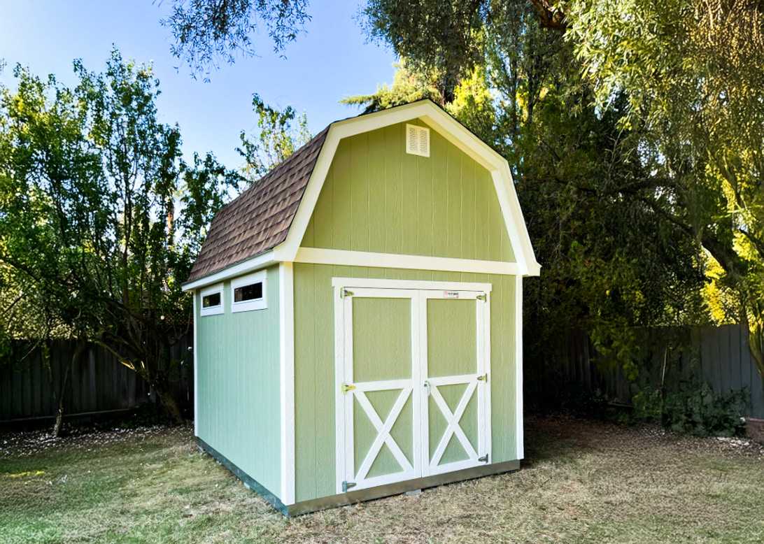 A green shed with a brown shingled roof, white trim, and double doors.