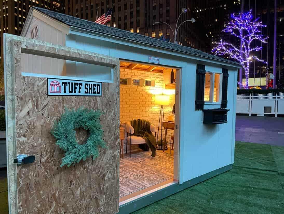 trade show staged as a cozy inviting hangout spot with the door wide open. We can see interiors of white style faux brick wall, a gray rug, desk and a chair
