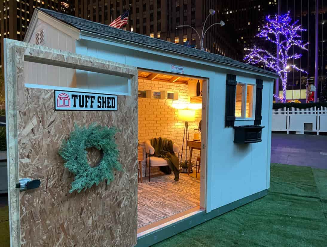 trade show staged as a cozy inviting hangout spot with the door wide open. We can see interiors of white style faux brick wall, a gray rug, desk and a chair