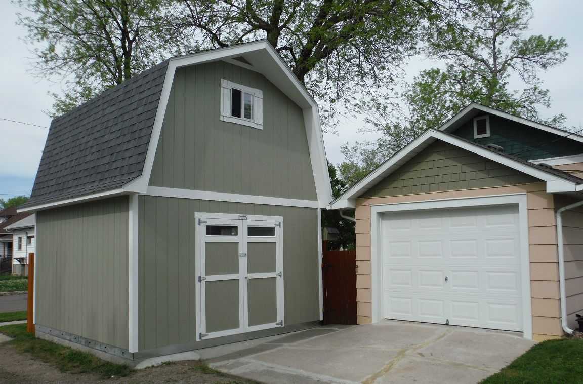 Exterior of 14X14 green TB-800 Tuff Shed barn next to a garage on a concrete pad