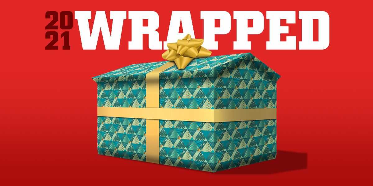 A gift box with green and gold triangle pattern, topped with a gold bow, against a red background with "2021 Wrapped" text.