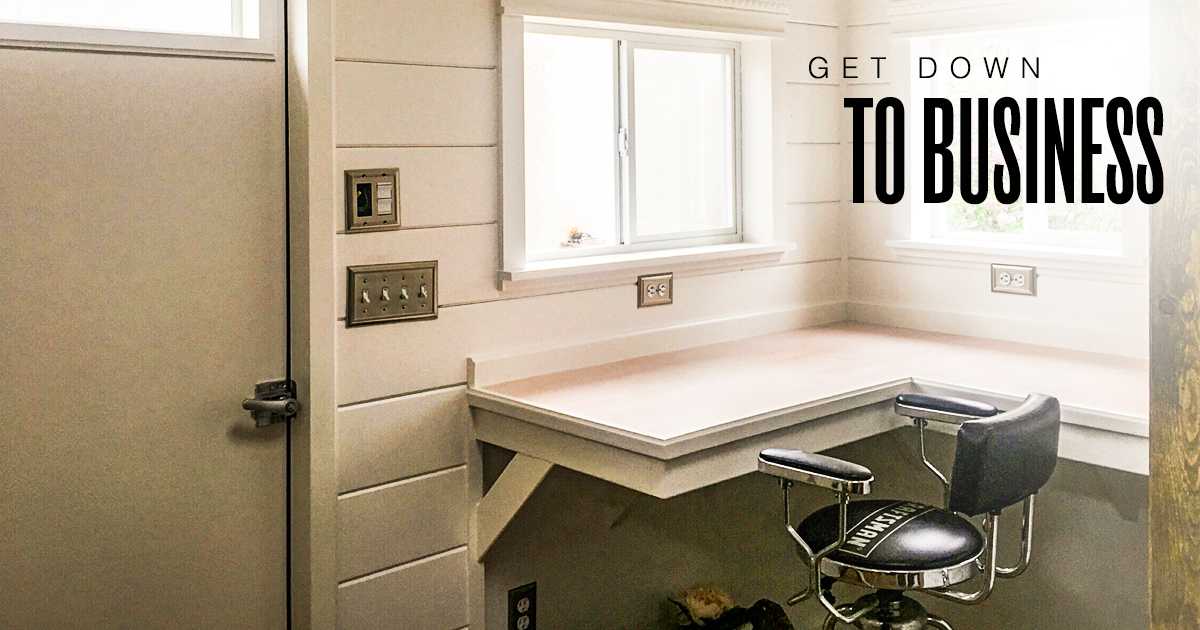 Home office corner with a wooden desk and swivel chair. White walls, window, and "Get Down to Business" text on the right.