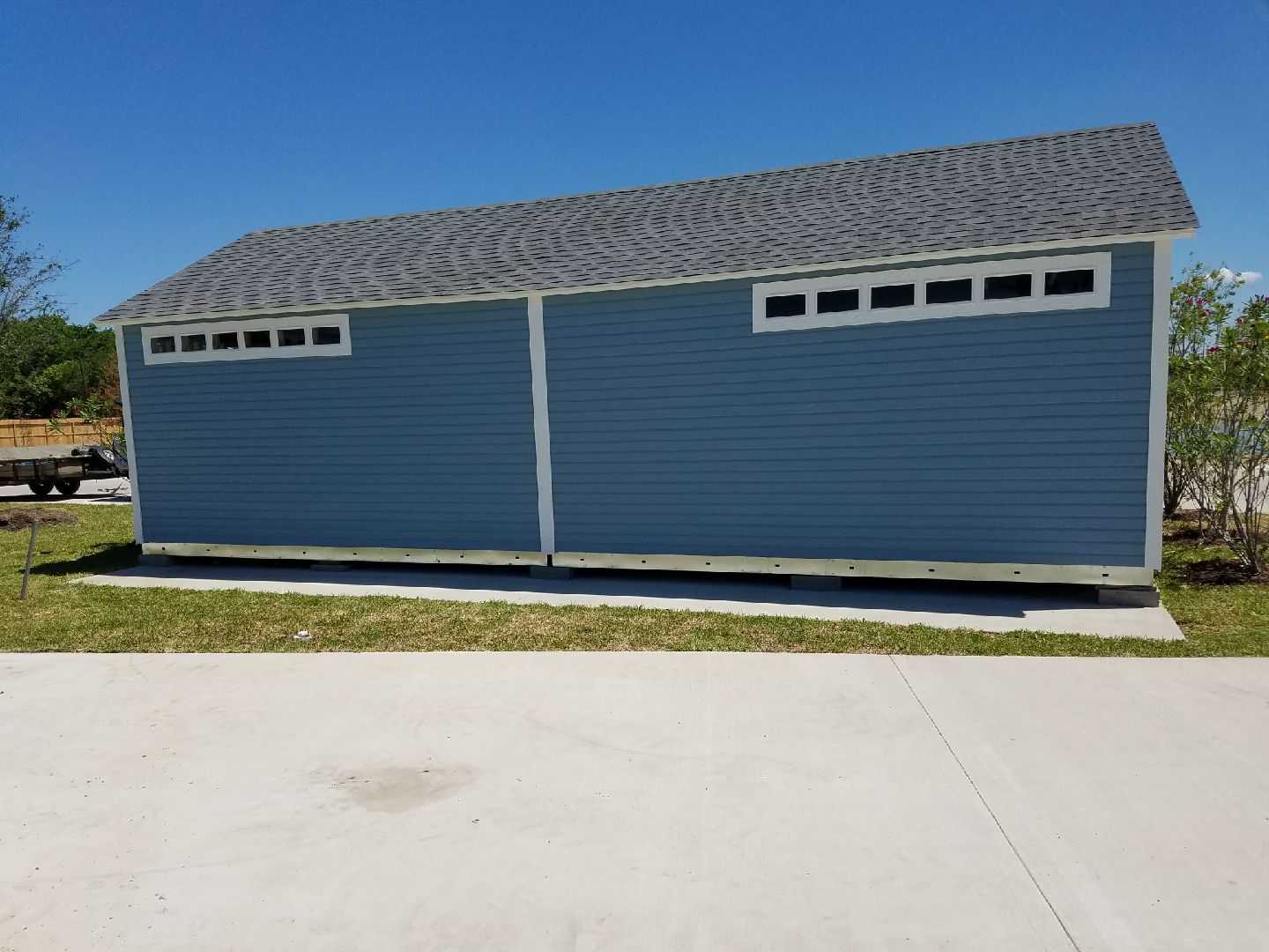 TR800 shed back view with a dark roof and small windows near the top, situated on a concrete surface with grass and trees in the background.