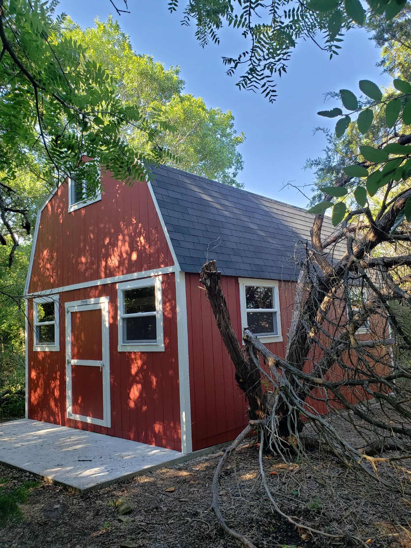 A red barn-style shed with white trim, nestled among trees, under a clear blue sky.