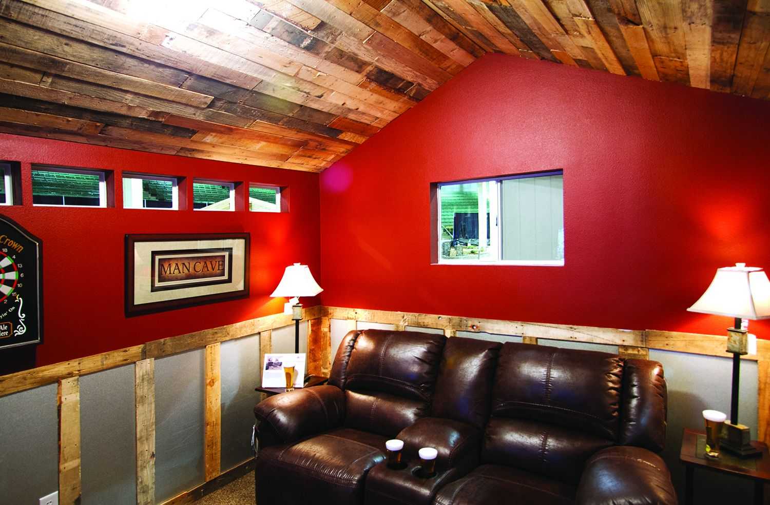 Cozy Shed with red walls, leather recliners, wooden ceiling, and lamps. "Man Cave" sign and small windows add character.