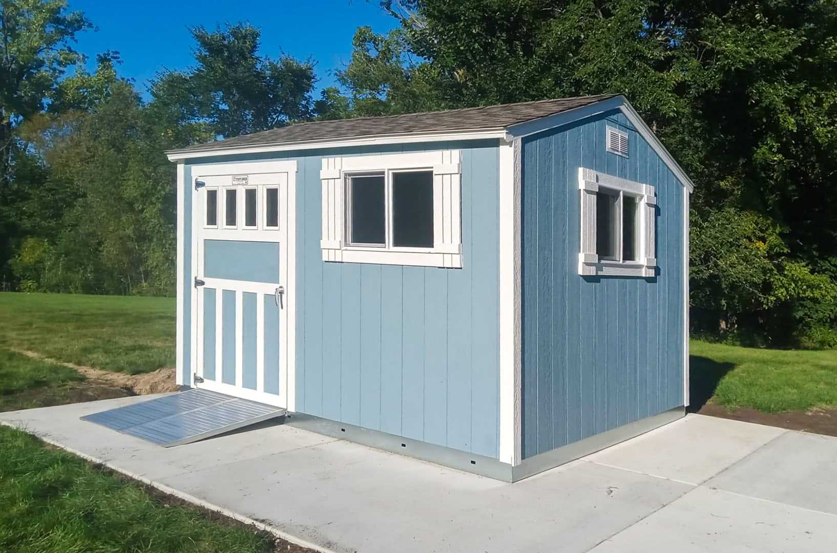 A TR700 blue shed with white trim and a ramp, situated on a concrete pad.