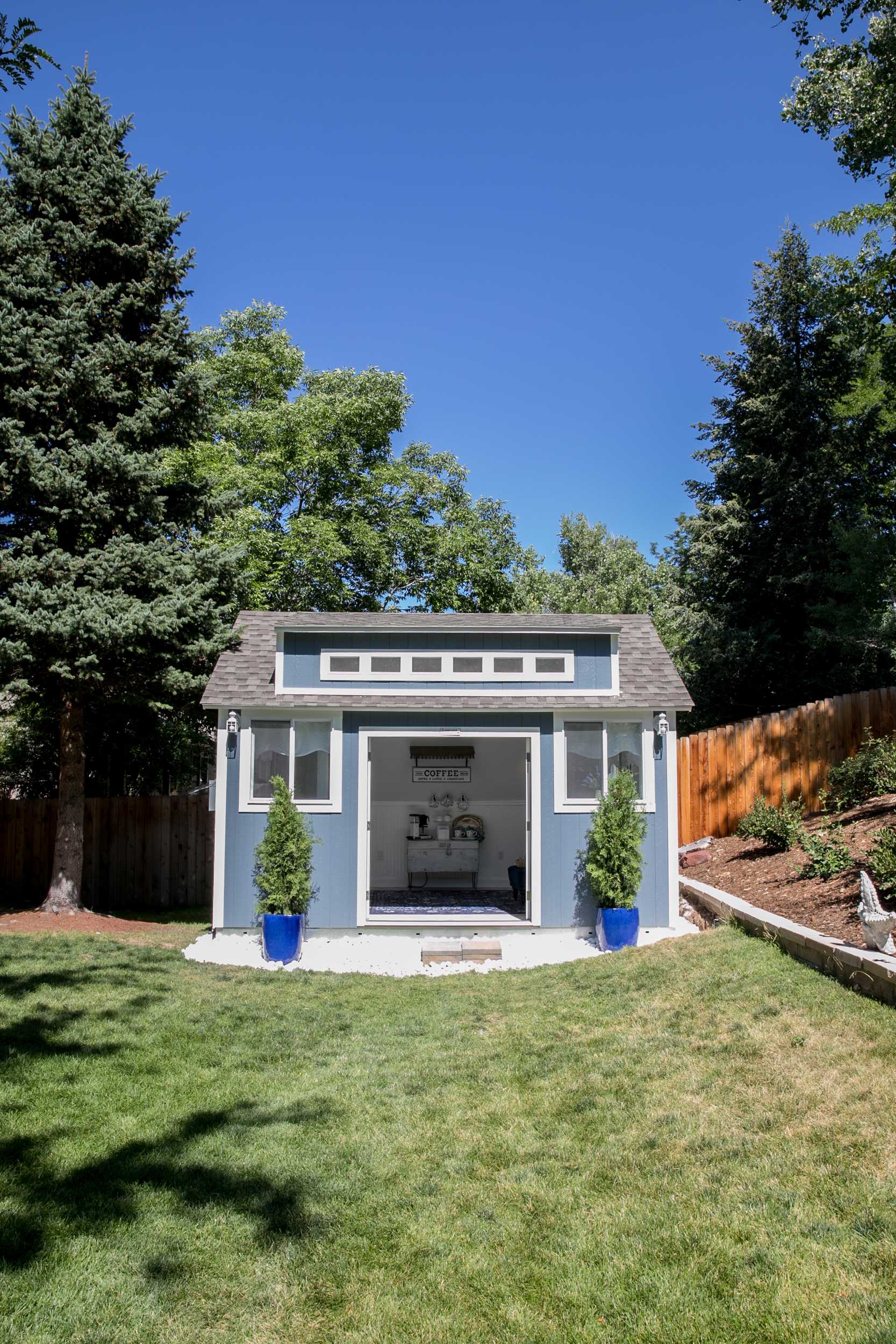 Linda's Exterior TR-800 She Shed 1 A blue and white TR800 shed with open doors, surrounded by trees and grass.