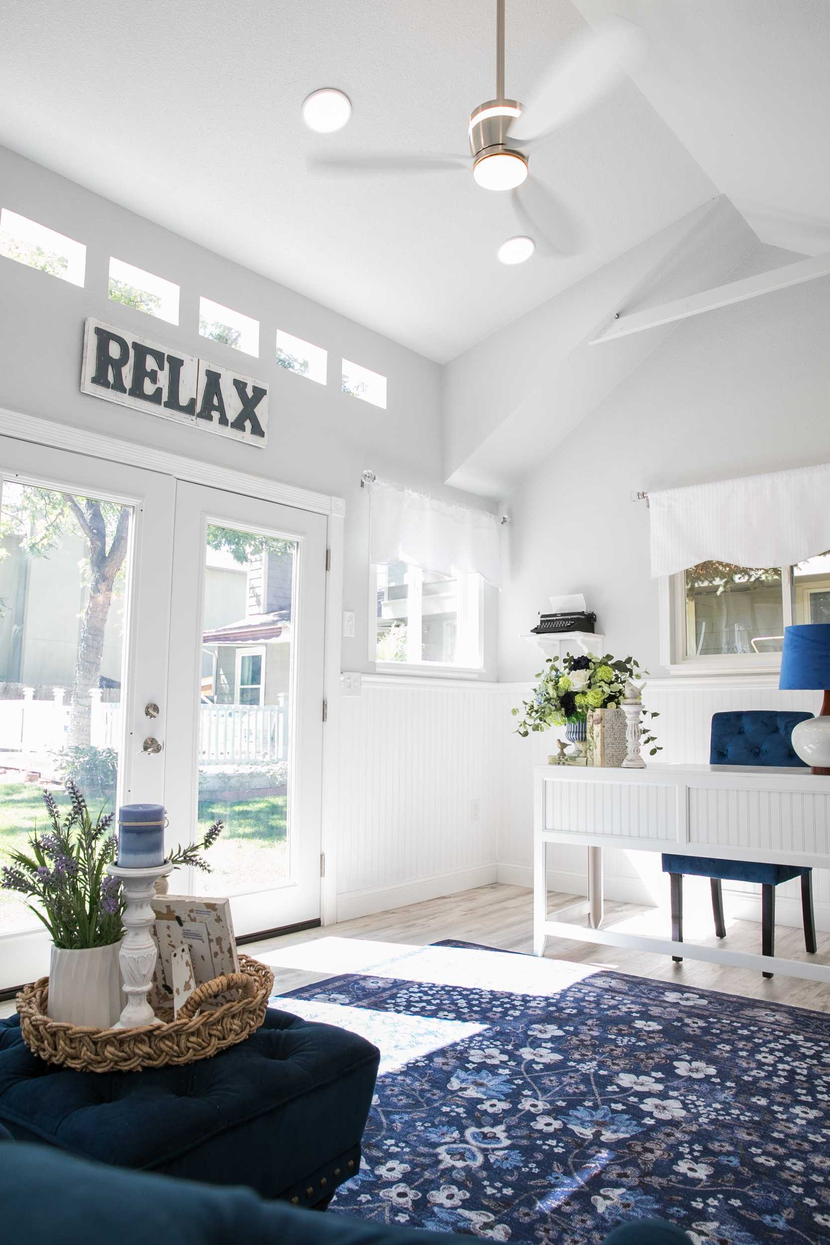 Linda's Interior TR-800 She Shed 2 Bright lroom with a blue floral rug, white furniture, large windows, and ceiling fan,.