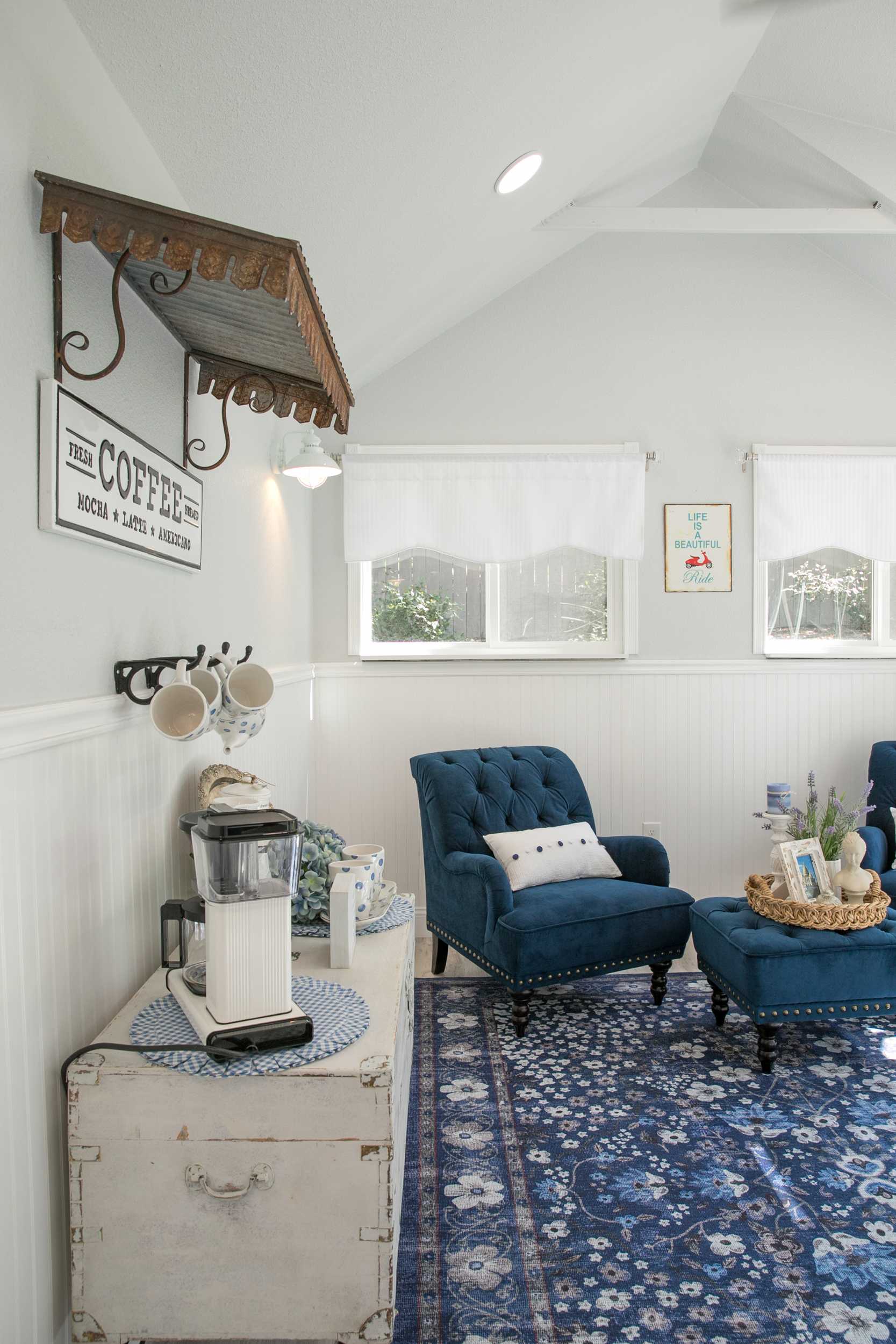 Linda's Interior TR-800 She Shed 4 Room with blue armchairs, a patterned rug, coffee station on a white chest, and wall art. Two windows let in natural light.
