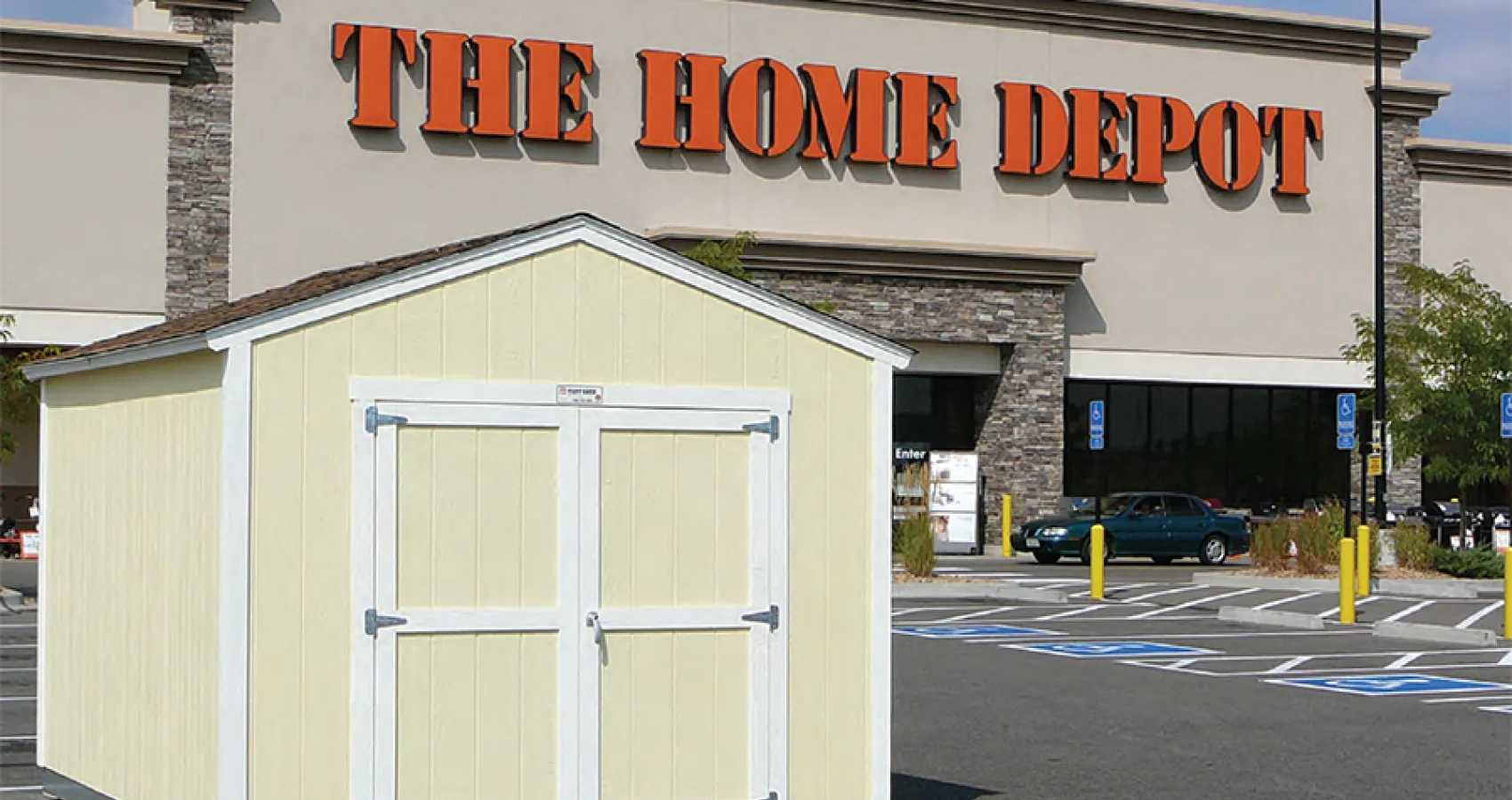 A yellow shed displayed in the parking lot of a Home Depot store, with reserved parking spaces visible in the foreground.