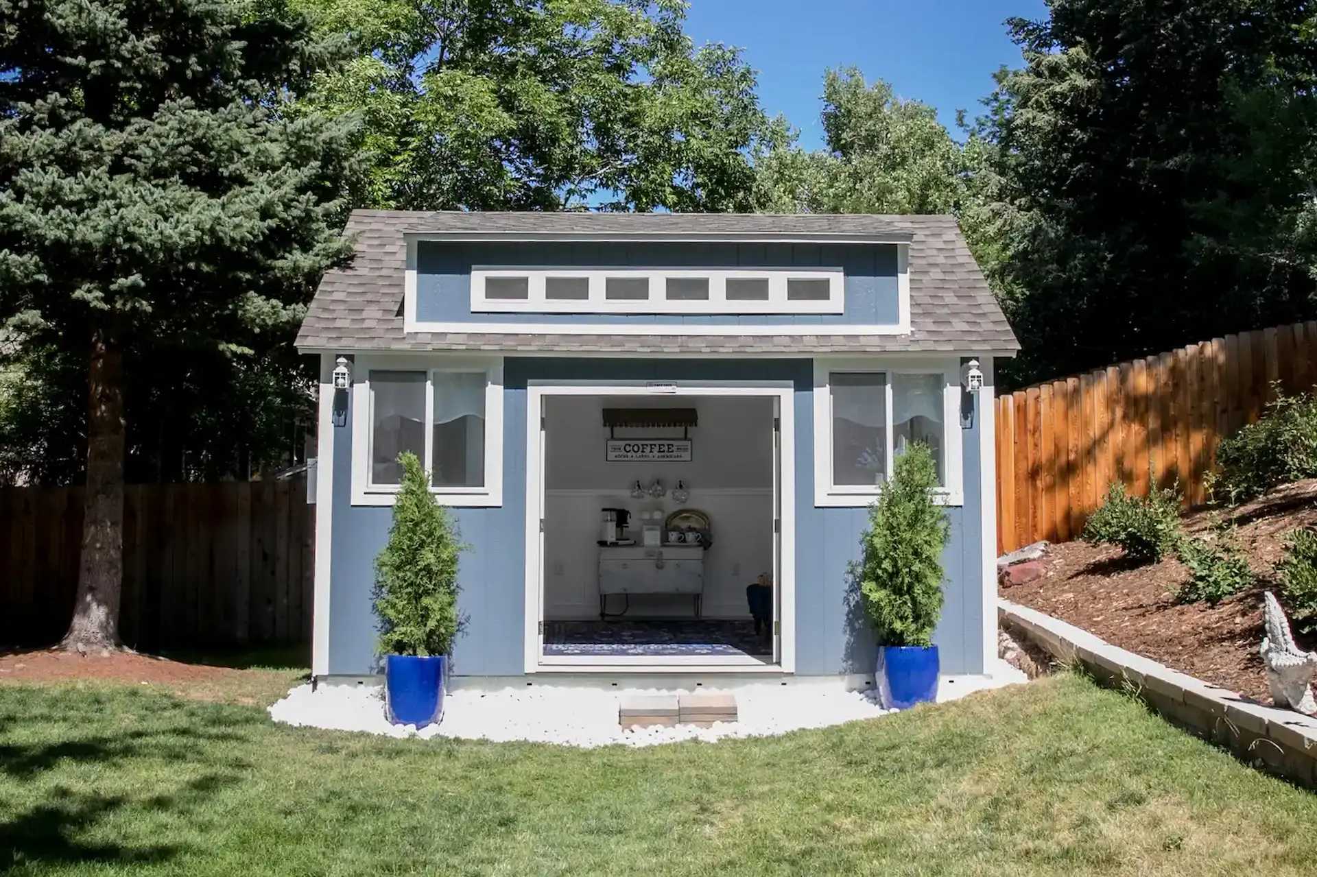 A blue and white TR800 shed with open doors, surrounded by trees and grass.