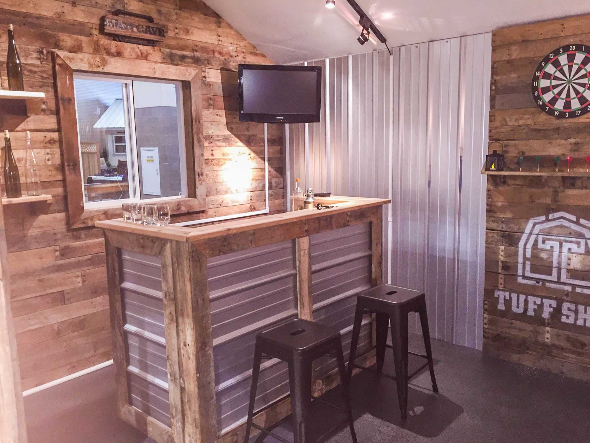 Interior photo of a Tuff Shed building with a bar, TV, two stools a dart board and a Tuff Shed logo