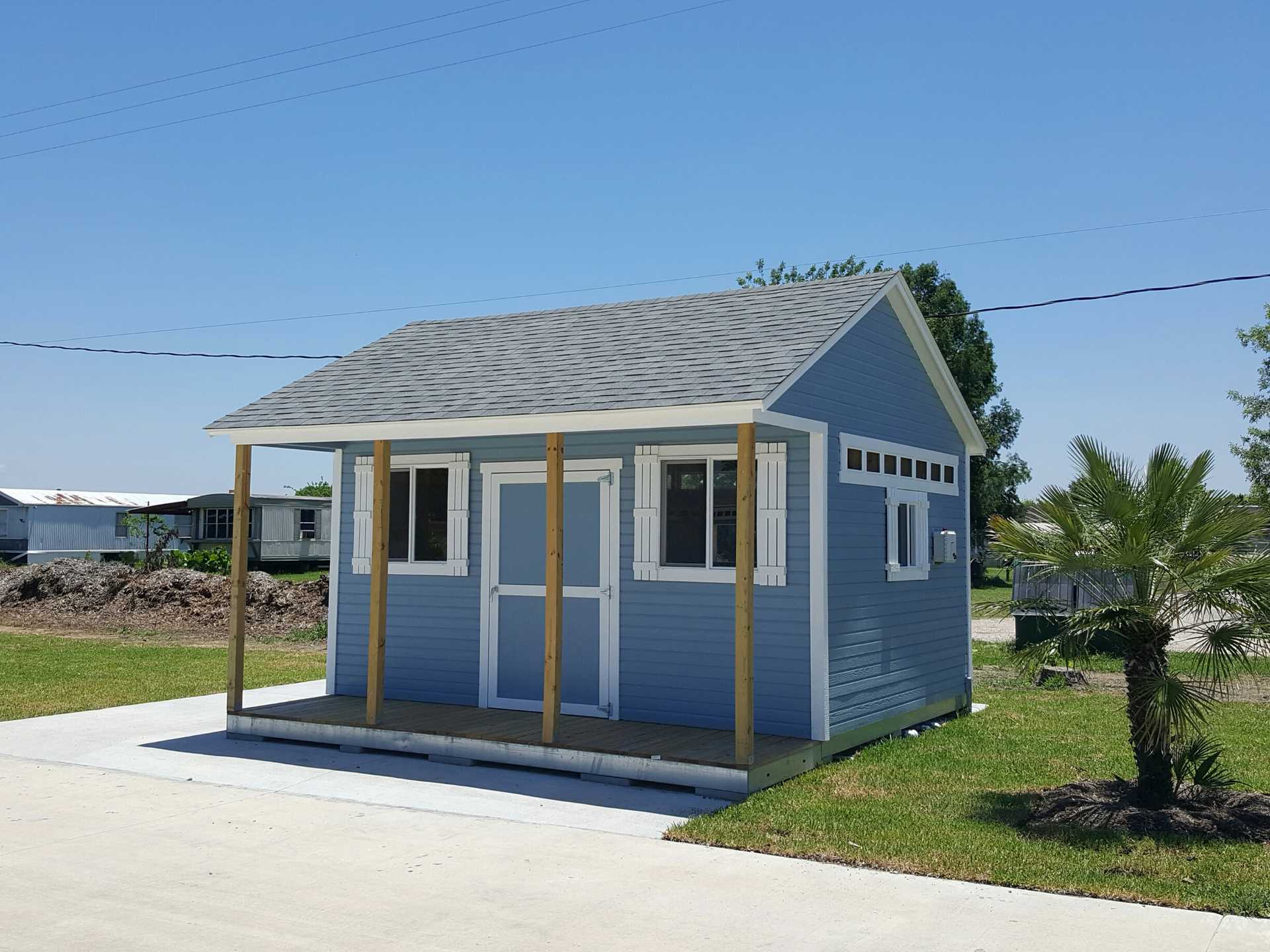 TR800 front shed with a gray roof and white trim, featuring a porch and surrounded by grass, under a clear blue sky.