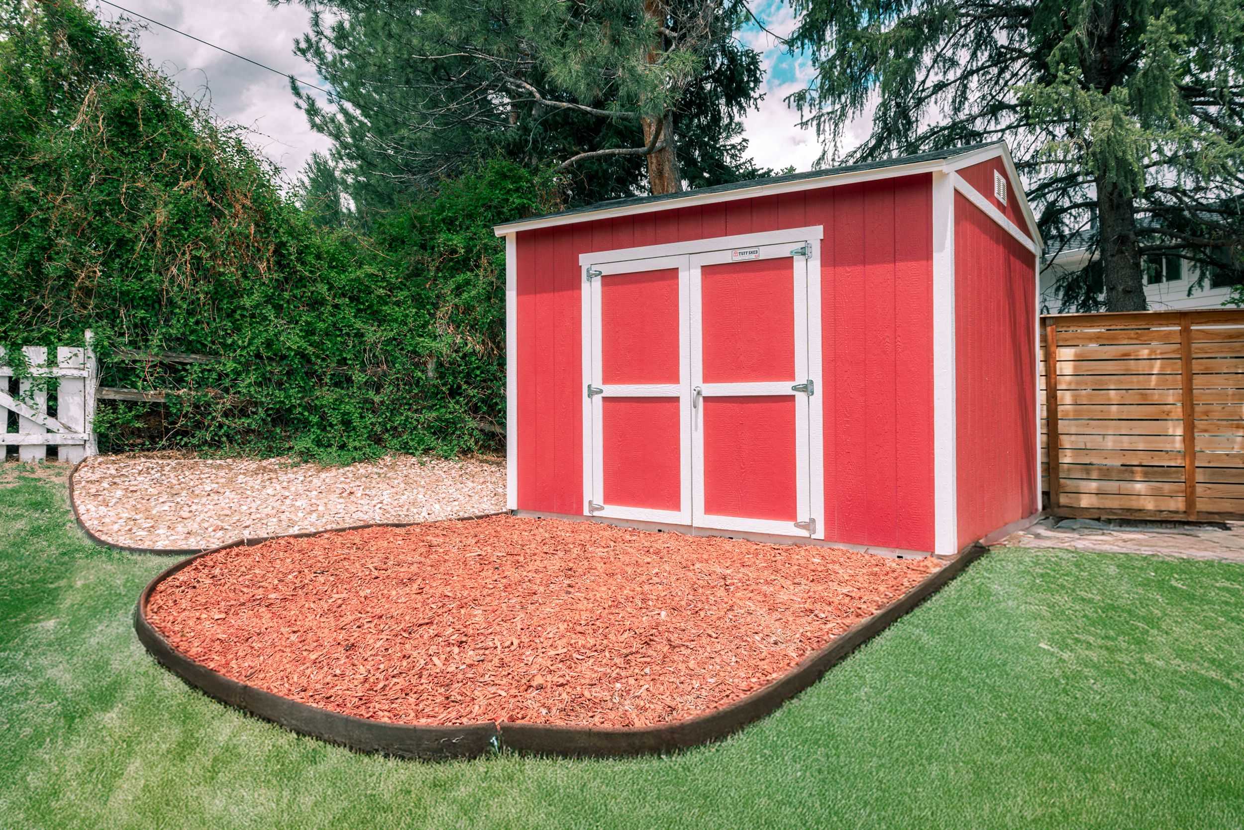 A red TR800 garden shed with white trim sits on a landscaped area with mulch.