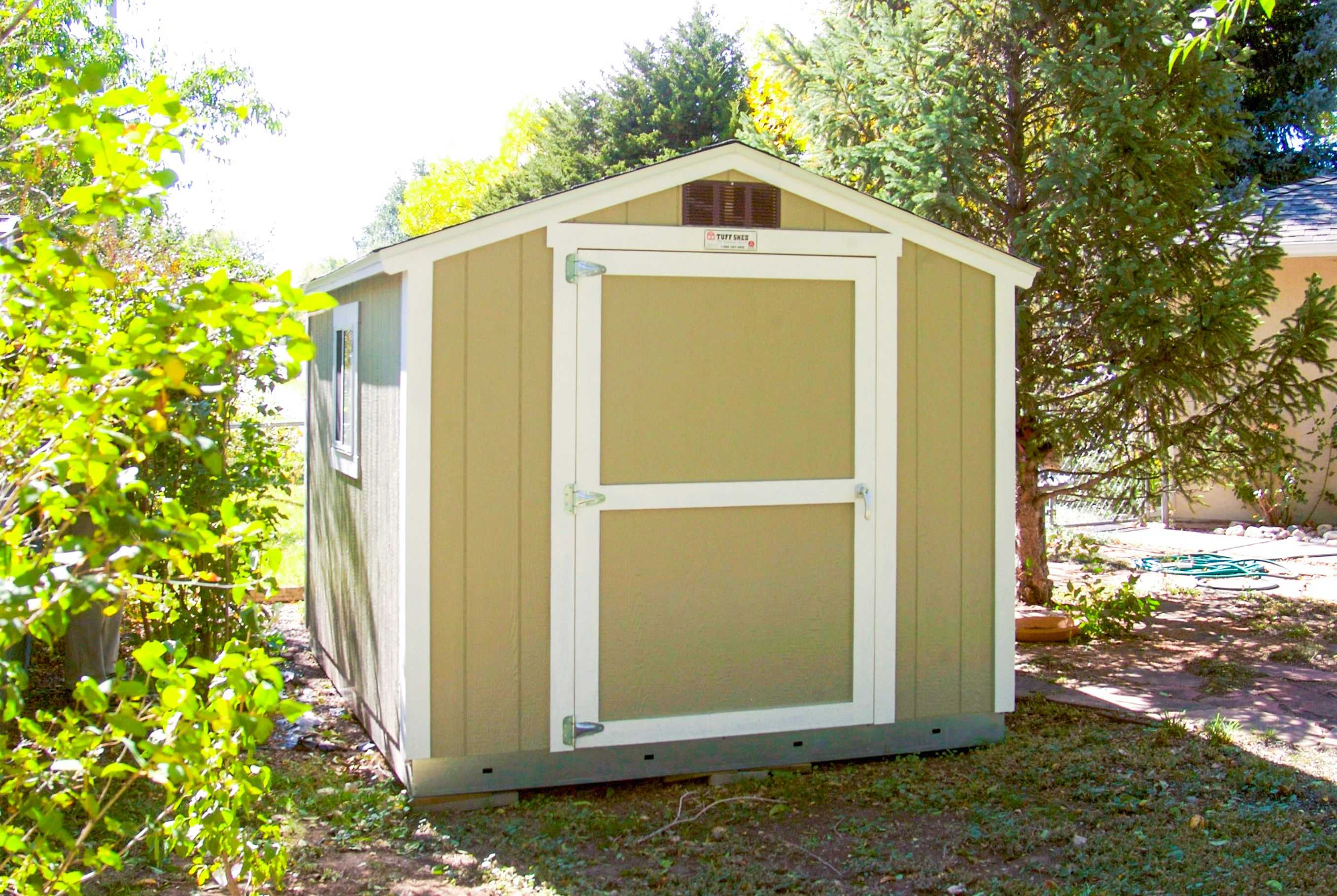 A SR600 shed with a white door and trim, surrounded by greenery and trees