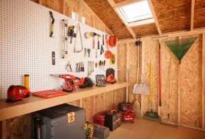 A well-organized workshop with tools on a pegboard, including drills, wrenches, and gardening tools, under a skylight in a wooden shed.