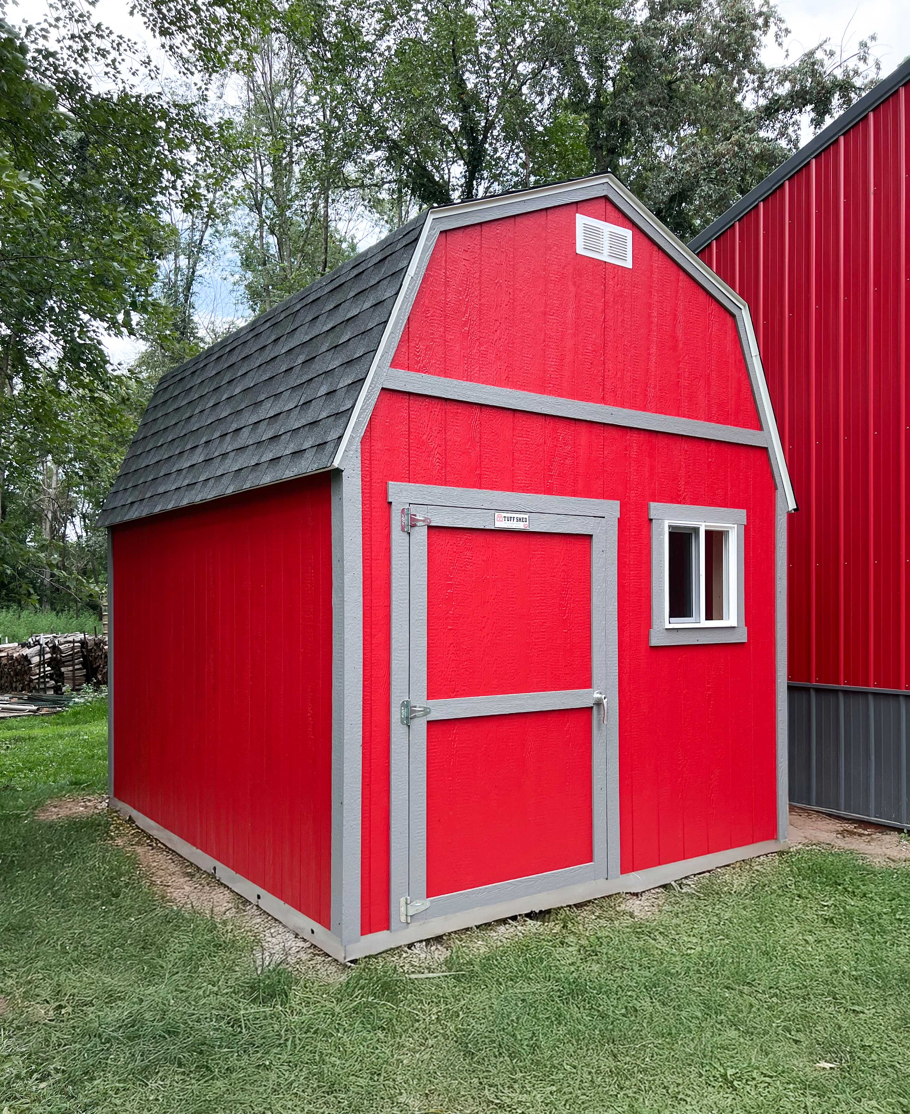 TB700 red barn with a gray shingled roof and white-trimmed door and window.