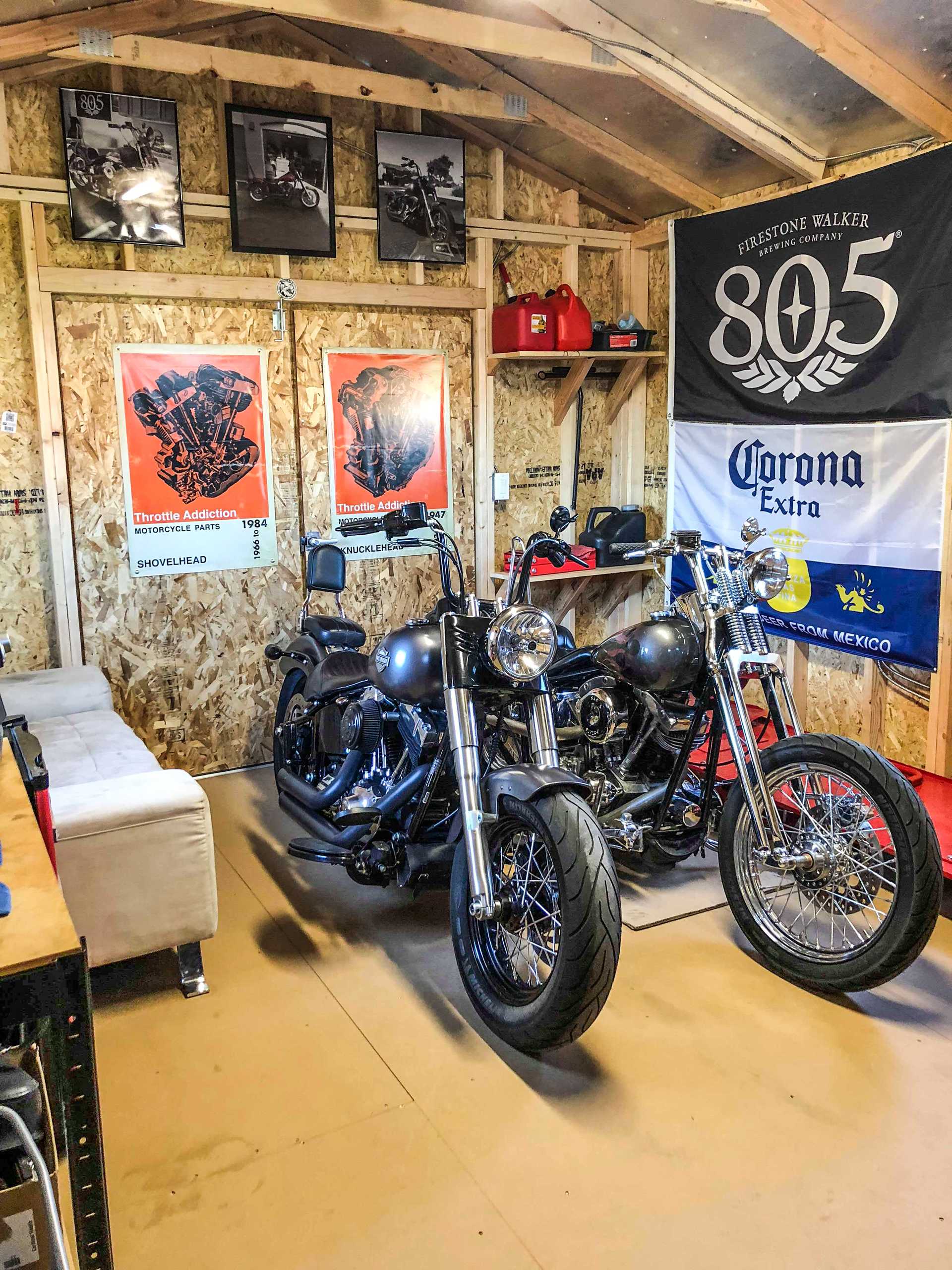 Two motorcycles in a garage with posters, a sofa, and banners on the walls