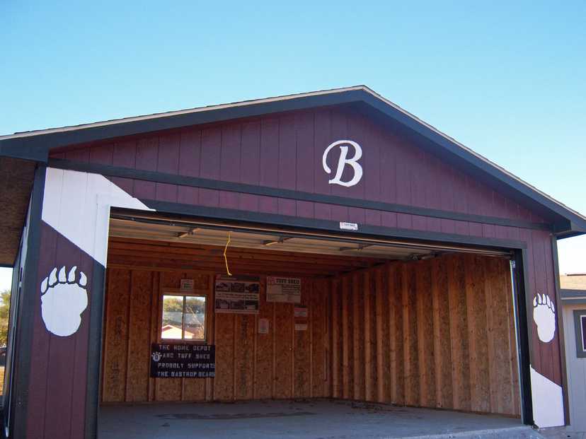 Open garage with a "B" on the front, bear paw prints on the sides, unfinished wooden interior, and a support sign for the Bastrop Bears.