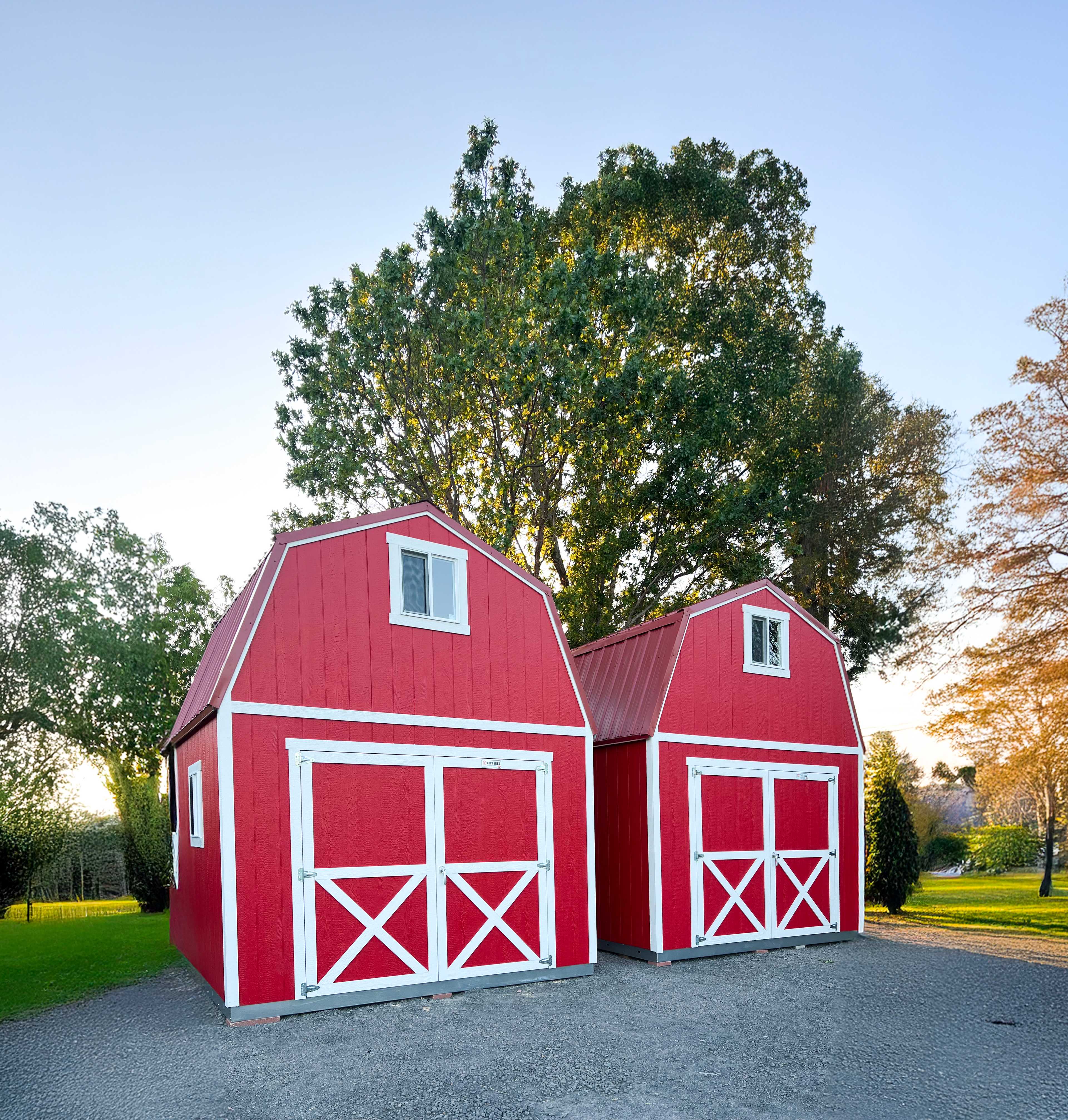 Two TB800 red barns with white trim stand side by side on gravel.