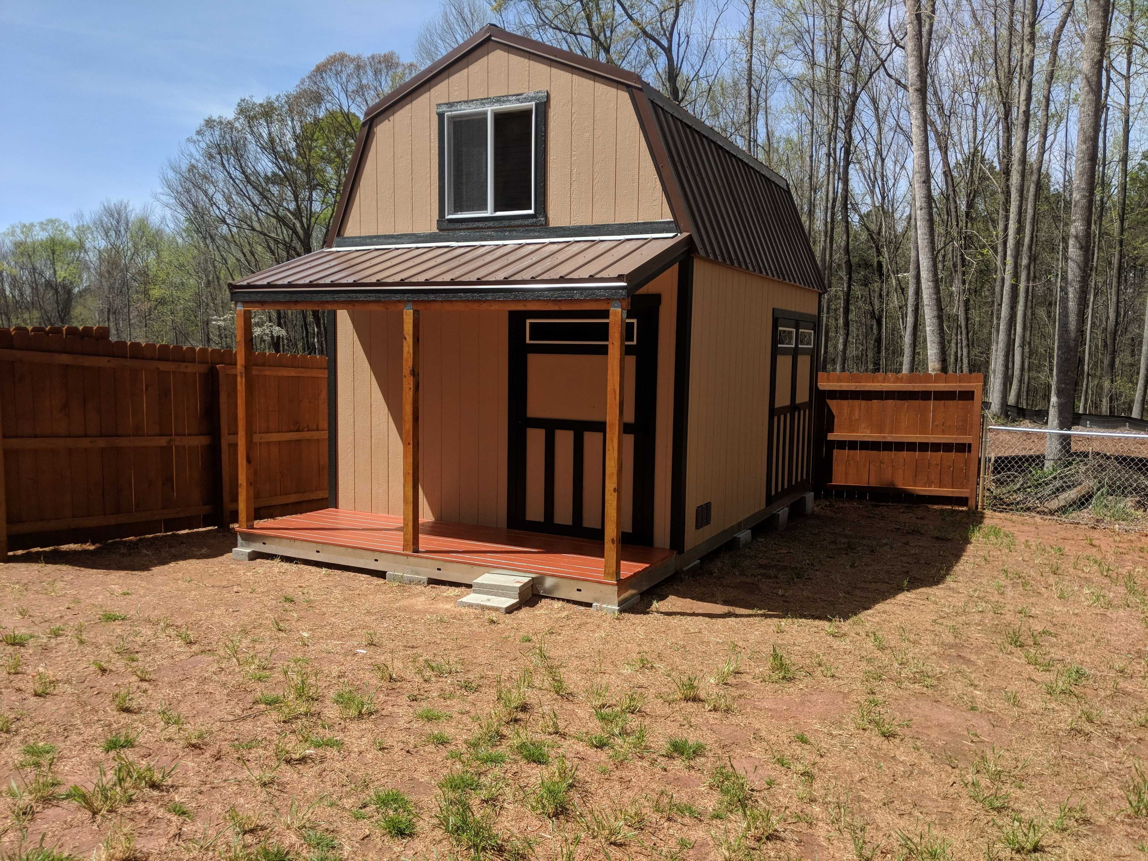 Exterior of a 12 X 16 Sundance TB-800 brown in color with a large window on top and a porch in front of a forest