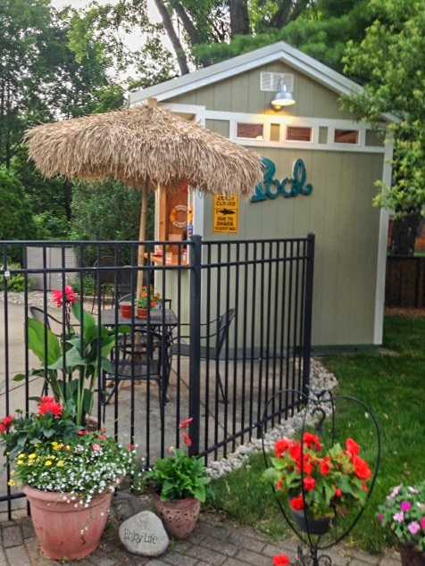 Poolside shed with a thatched umbrella, chairs, and potted flowers