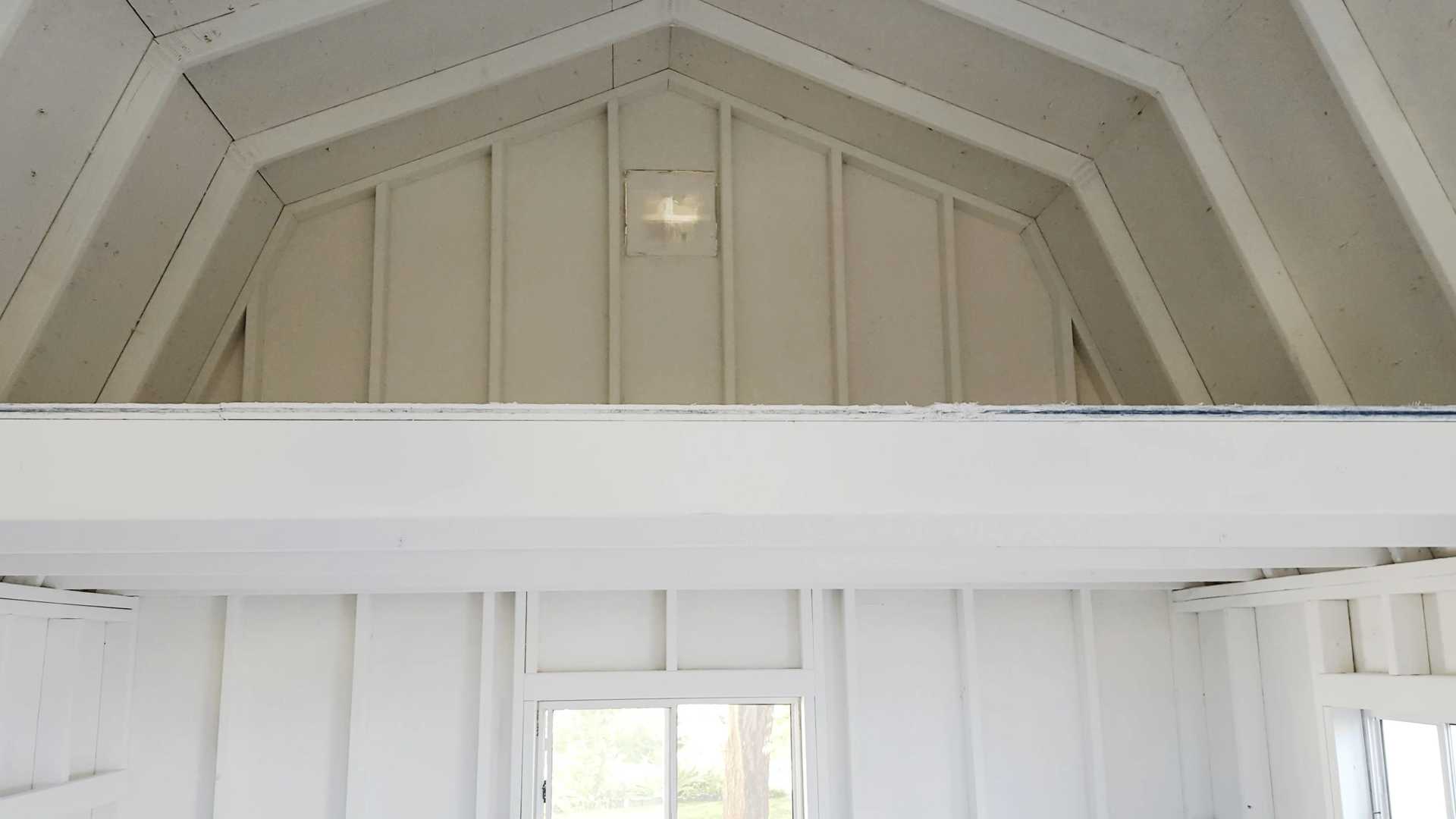 Interior of a white, vaulted ceiling room with a small window below. Natural light illuminates the space, highlighting wooden beams.