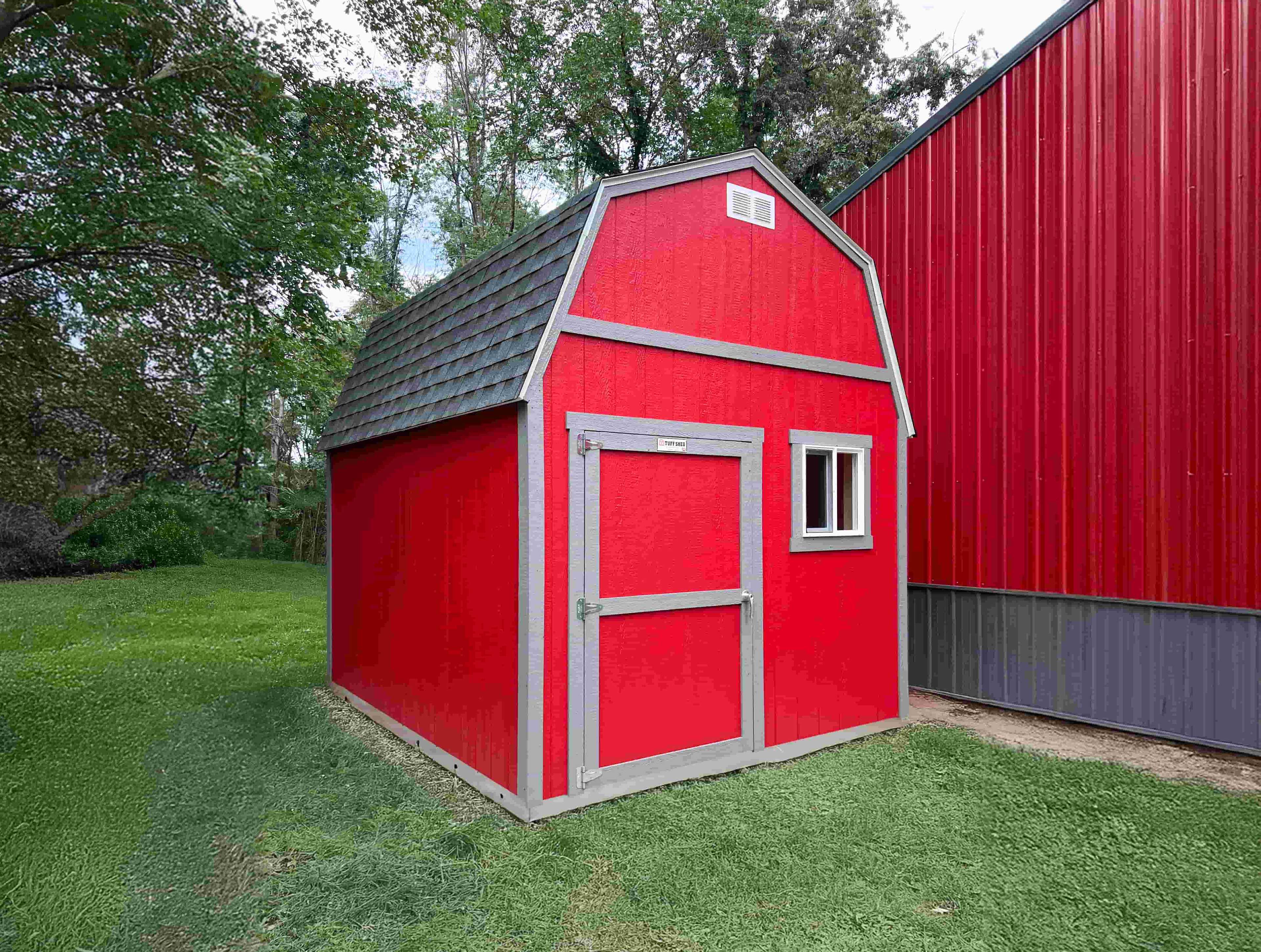 TB700 red barn with a gray shingled roof and white-trimmed door and window.