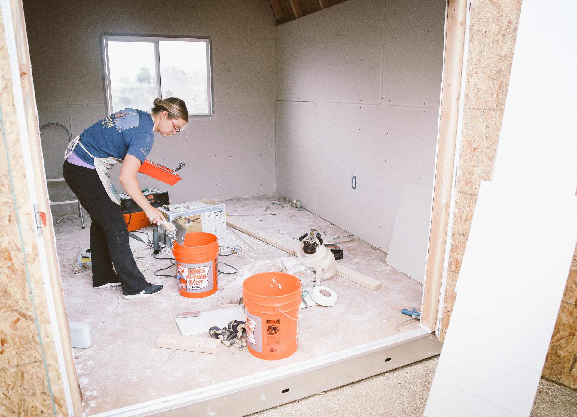 Michaela finishing out the interior of her new TB-700 1 A woman mixing up the drywall in two big buckets wearing a blue shirt and apron, with a window in the background.