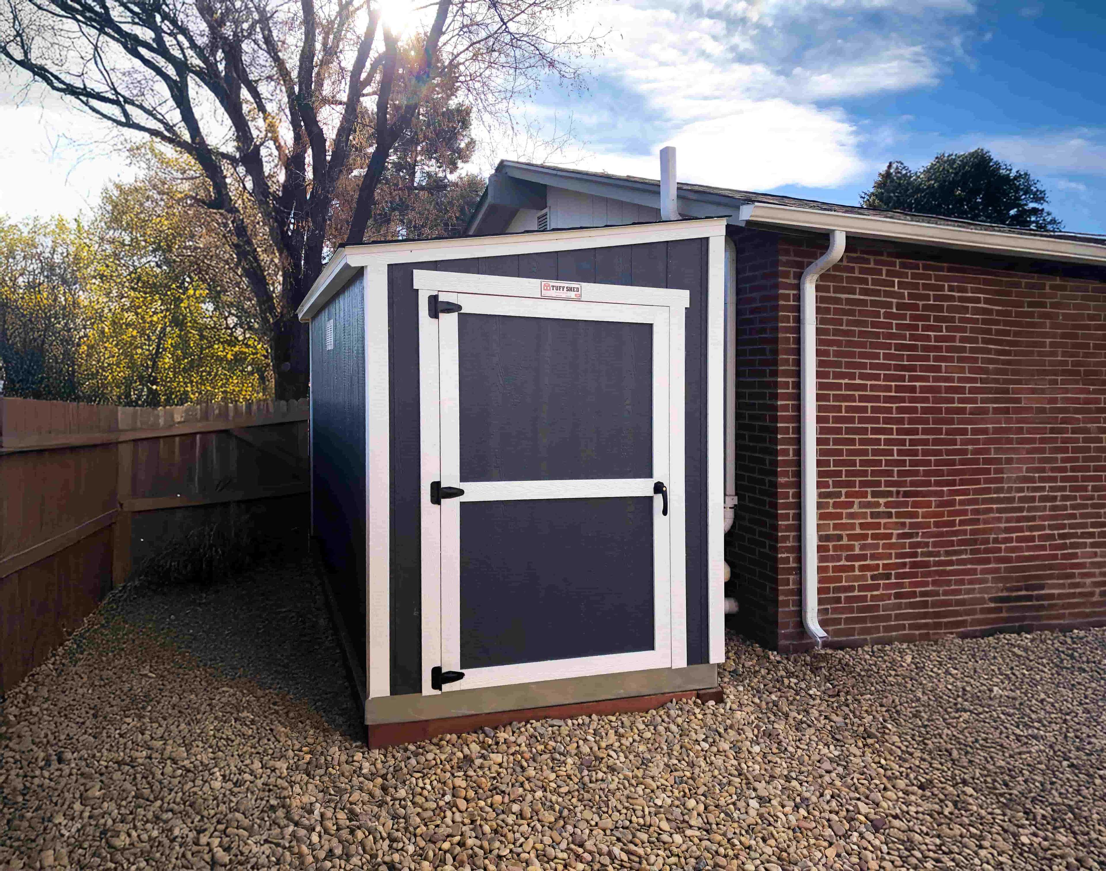 A black lean-to style shed with white trim tacked away in the narrow backyard