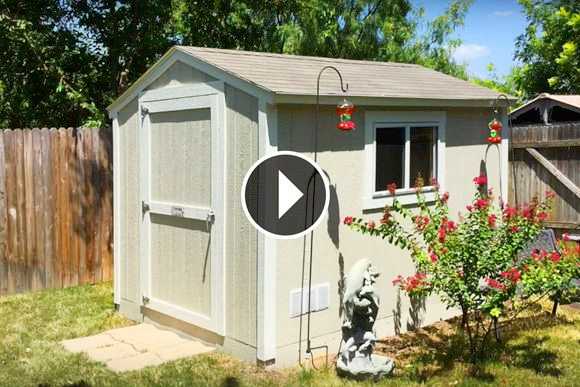 SR600 shed with a window and door, surrounded by grass and a flowering bush. A statue and bird feeders are nearby.
