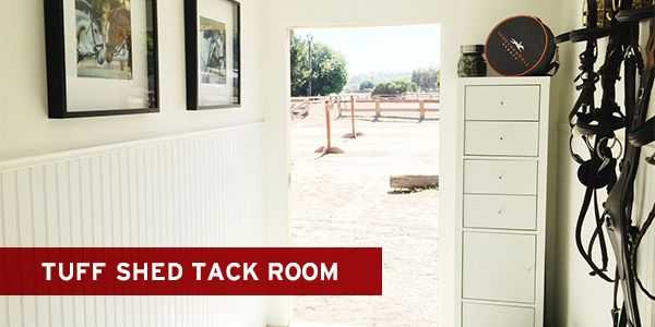 Bright tack room with white cabinets, equestrian gear, and picture frames on walls, opening to a sunny outdoor area with fences.