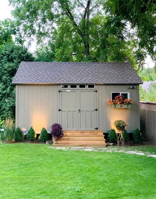 ATR800 garden shed with gray siding, lit by ground lights, surrounded by greenery, with a flower box under a window and a wooden step entrance.