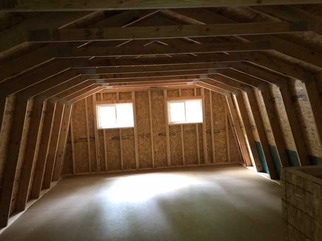 Second floor interior with exposed wooden beams and two small windows allowing natural light to enter.
