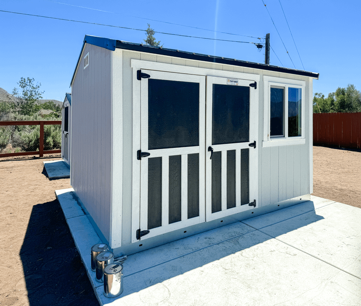A SR600 white shed with black doors, situated on a concrete slab, with a clear blue sky in the background.