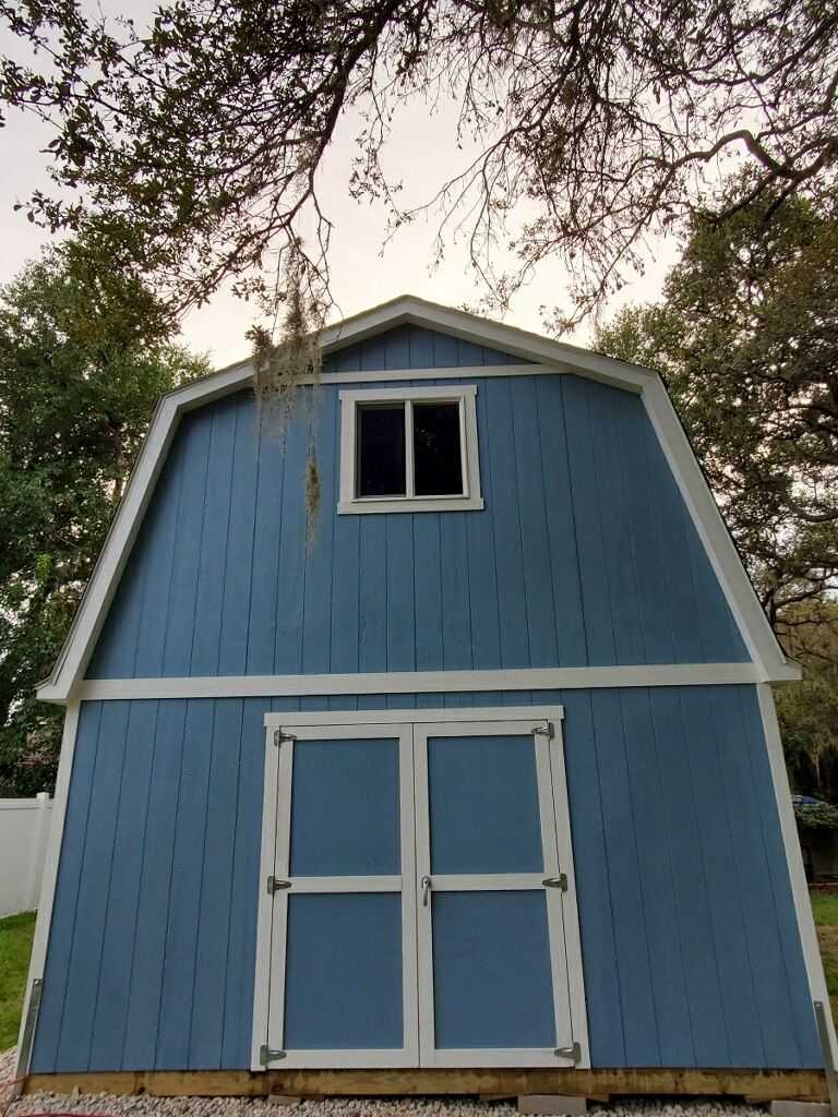 Blue TB800 shed with white trim, double doors, and a small window, surrounded by trees and a white fence.