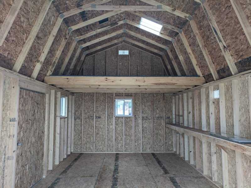 Interior of an unfinished TB700 wooden shed with a loft, exposed beams, and small windows