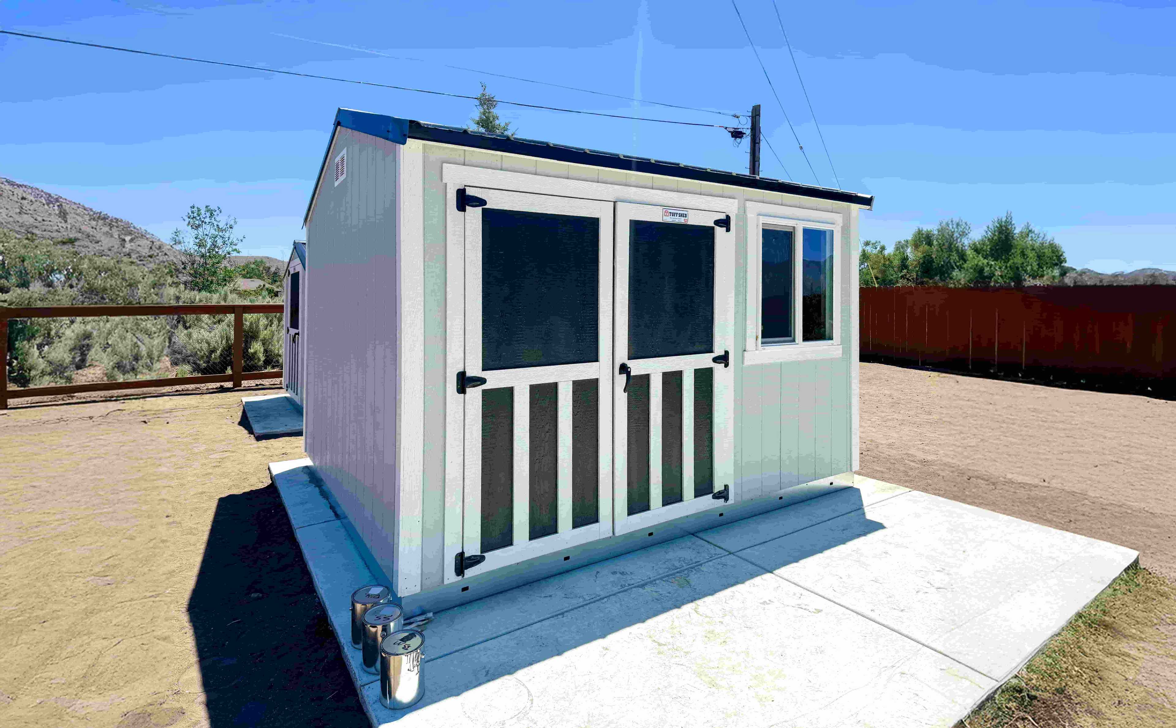 A SR600 white shed with black doors, situated on a concrete slab, with a clear blue sky in the background.