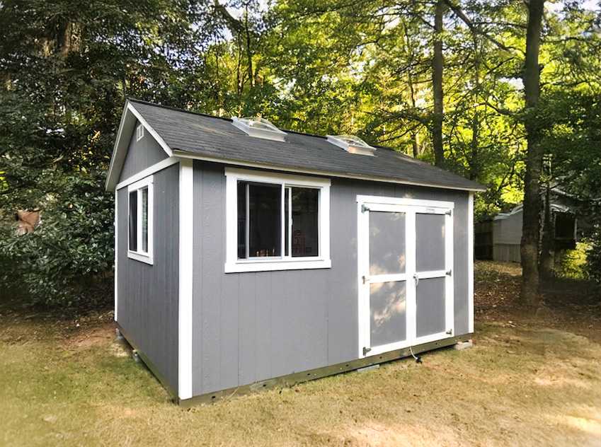 A gray TR800 garden shed with white trim, two windows, and double doors, set on grass with trees in the background.