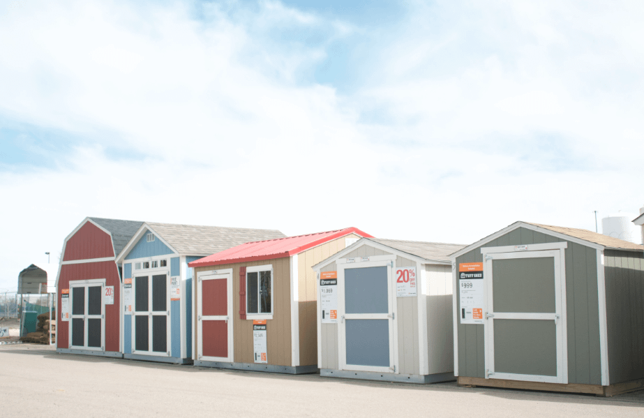 A row of colorful storage sheds displayed outdoors, each with a price tag. The sky is clear with a few clouds.